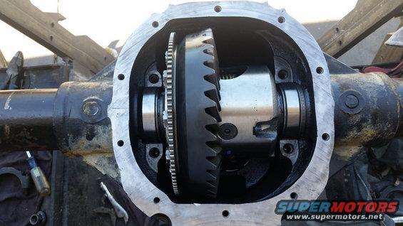 Open differential housing with gears and bearings visible. Tools and rags are on the ground nearby