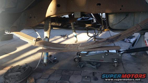 Leaf spring assembly supported by a jack and jack stands, with a drum brake visible
