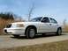 2000 Ford Crown Victoria - A white 2000 Ford Crown Victoria sedan is parked on the side of a road with dry grass and trees in the background.
