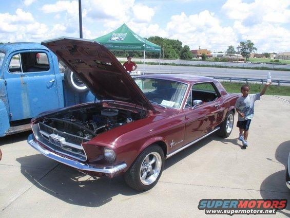 Maroon 1967 Ford Mustang coupe, hood open, parked next to blue truck