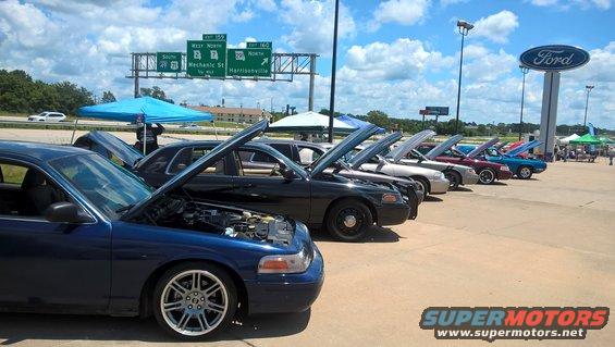 Blue 2004 Ford Crown Victoria in foreground, hoods open on multiple cars