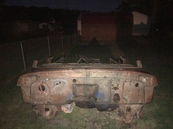 Rusted vehicle front end with exposed engine bay, wires visible, sitting on grass