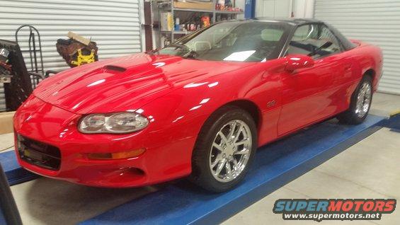 Red sports coupe with a black t-top roof, parked on a lift in a garage