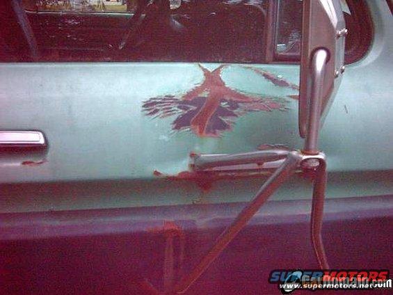 Close-up of a light green car door showing rust damage and a faded decal; side mirror assembly visible