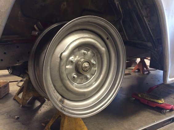 Close-up of a silver steel wheel on a car's suspension, supported by jack stands