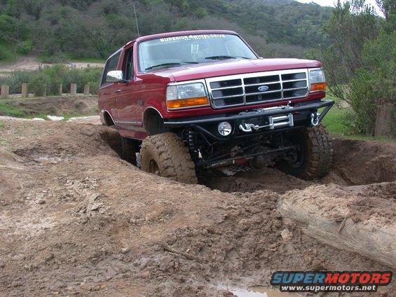 1996 Ford Bronco navigating a muddy off-road trail, front bumper with winch visible