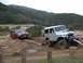 1996 Ford Bronco - Two off-road vehicles navigate a muddy terrain with hills in the background.