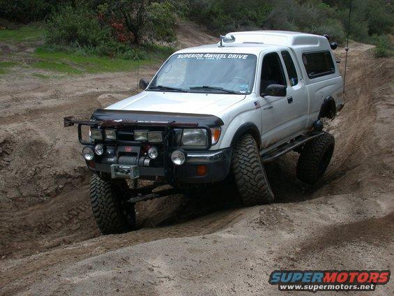White Toyota Tacoma with off-road modifications on a dirt trail
