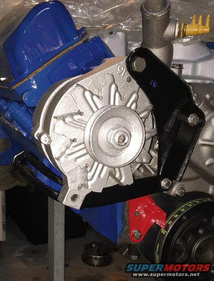 Close-up of an alternator mounted to an engine block with blue valve covers. A red bracket is visible below the alternator