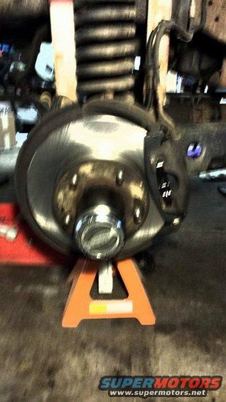 Close-up of a vehicle's front brake rotor and hub assembly supported by an orange jack stand