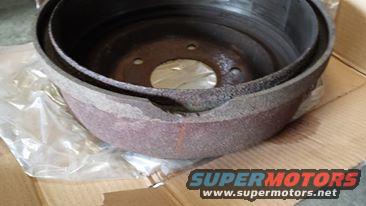 Rusty brake drum with visible damage, resting on plastic and cardboard