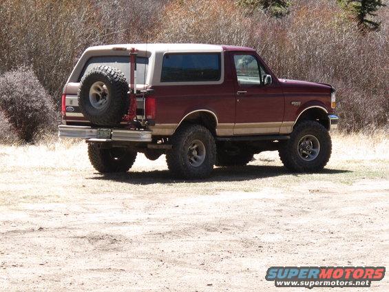 Maroon Ford Bronco with tan top and spare tire on back, parked on dirt