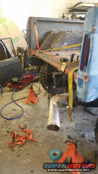 Blue 1978 Ford Bronco rear quarter panel and bed, on jack stands, with exhaust pipe and straps