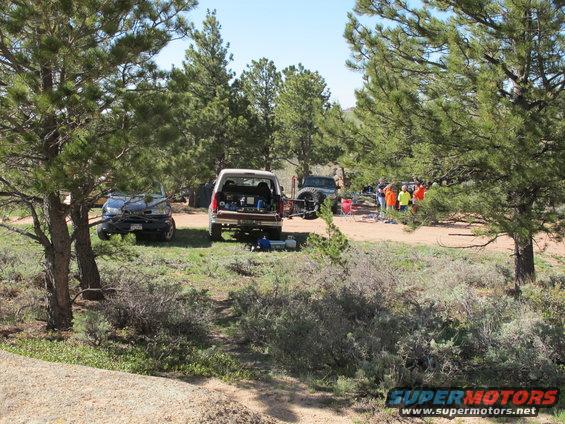 Several off-road vehicles parked in a wooded area with people gathered around