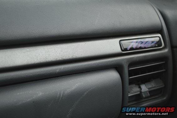 Interior dashboard trim with a dark badge showing purple lettering