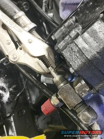 Mechanic using vise grips on a hydraulic fitting connected to a black component