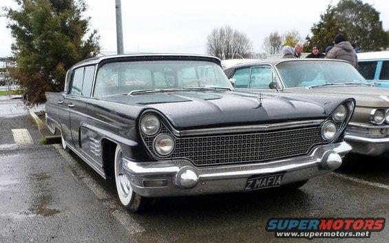 Front view of a dark sedan with a large grille and dual headlights. License plate reads 'Z MAFIA'. Another car is parked next to it