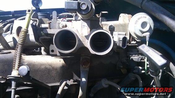 Engine throttle body with dual openings and various sensors. Oil cap visible