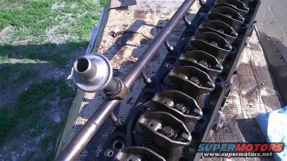 Engine cylinder head with rocker arms and a fuel rail assembly. The head is black and appears to be made of metal
