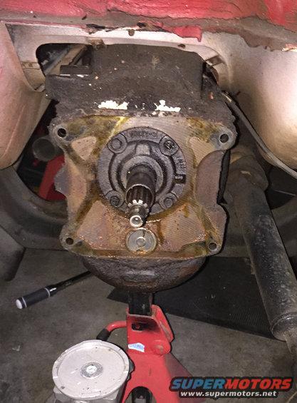 Close-up of a rusty transfer case with a splined shaft protruding. Supported by a red jack stand