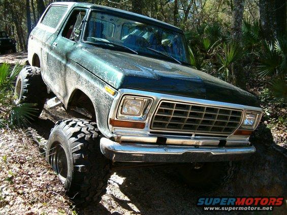 Green Ford Bronco with large tires on a dirt trail, another vehicle in background