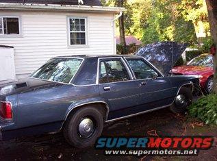 Dark blue sedan parked next to a house, hood up on a red car behind it