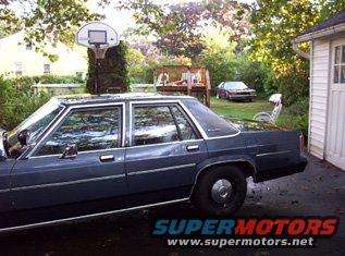 Dark blue 1980s Ford Crown Victoria sedan, side view, parked in driveway next to garage