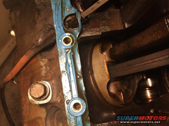 Engine gasket with blue sealant and metal grommets, next to engine block and crankshaft
