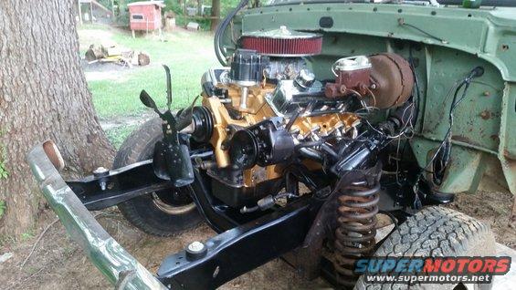 Engine and chassis of a green vehicle, with gold-colored engine components and black frame. Tires and suspension visible