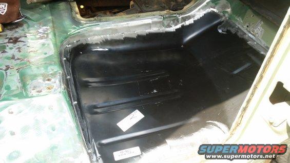 Interior floor pan of a vehicle undergoing repair, showing new black metal paneling and green primer
