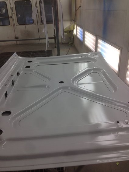 Underside of a white car hood with reinforcing ribs, in a paint booth