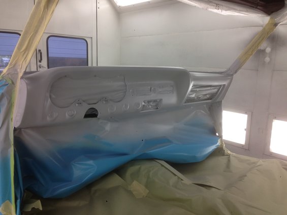 Car dashboard covered in primer, masked off for painting in a booth