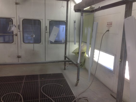 paint booth with parts hanging to be painted, including a metal panel and some trim pieces