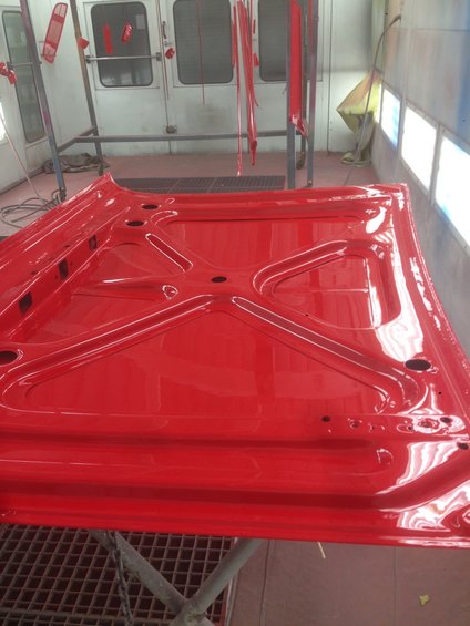 Underside of a red car hood, freshly painted, in a paint booth