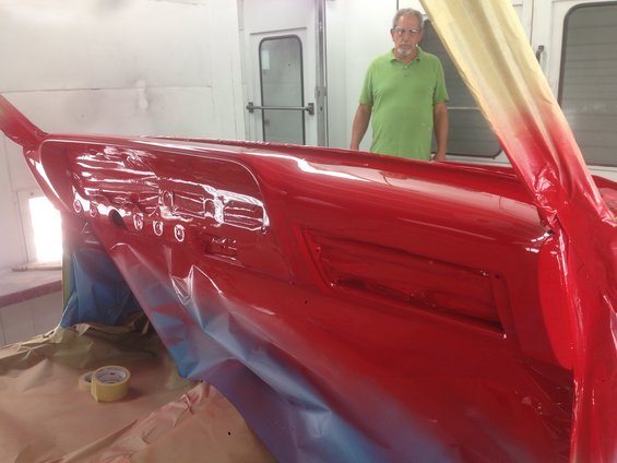 man in green shirt stands behind shiny red car dashboard being painted