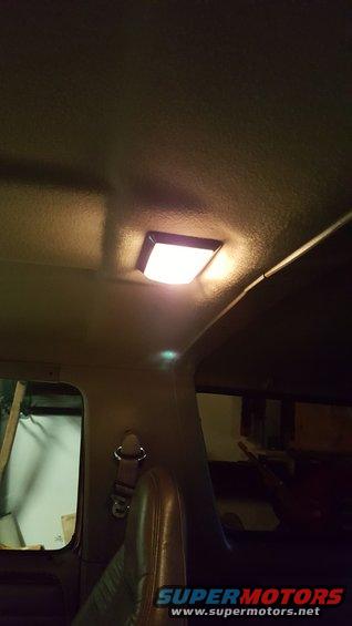 Interior overhead light in a dark vehicle, showing a seatbelt anchor and part of a seat