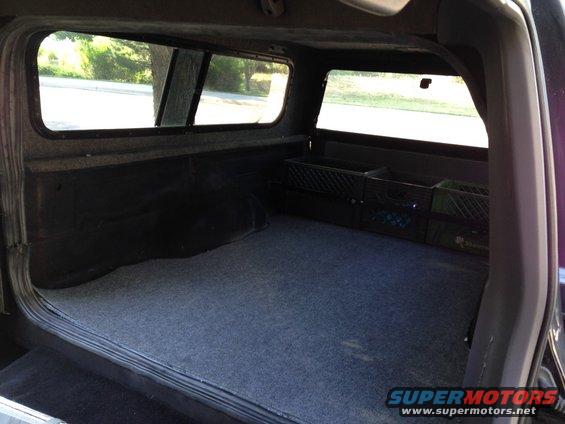 Truck bed interior with carpet, black plastic crates, and windows of a camper shell