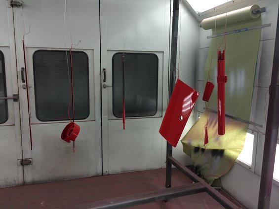 Red car parts hanging in a spray booth, ready for finishing