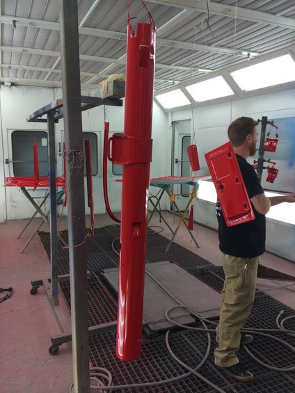 Red car door and other parts hanging in a paint booth, a man stands nearby