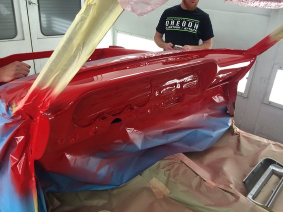 Red dashboard and interior panels being painted in a spray booth