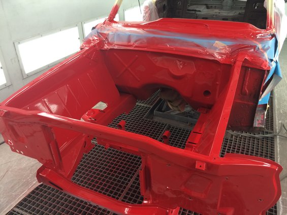 Red car body in a paint booth, showing the engine bay and front frame