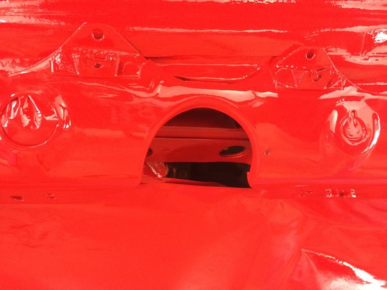 Close-up of a red painted car frame with mounting brackets and an arched opening