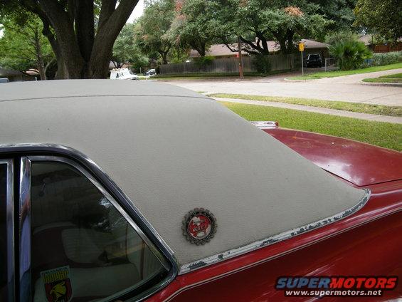 Close-up of a red car's vinyl top and rear quarter panel, showing a circular emblem