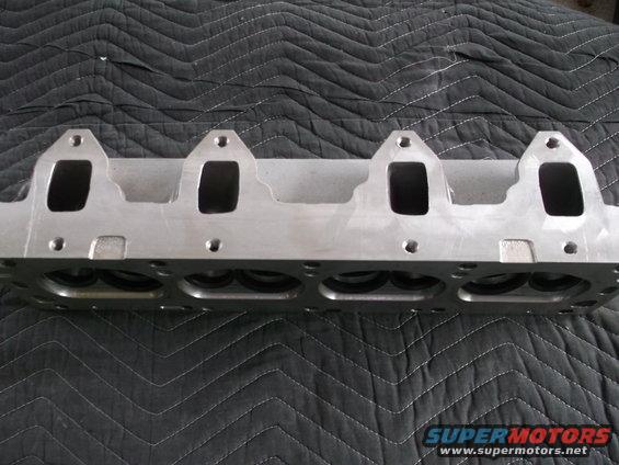 Engine cylinder head with four intake ports visible, resting on a quilted black surface