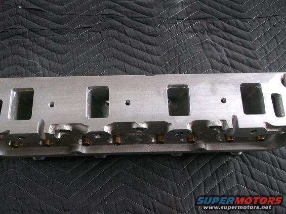 Aluminum engine cylinder head with rectangular intake ports, resting on a black quilted mat