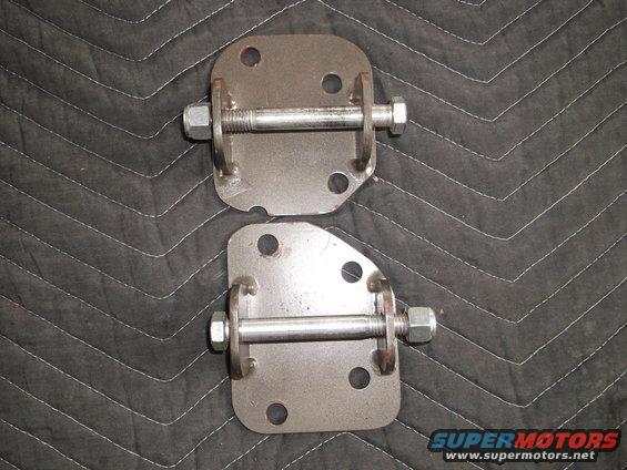 Two metal brackets with bolts and nuts, laid on a quilted black surface