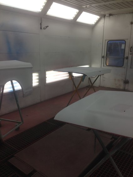 Car hoods and a fender primed in a white paint booth with overhead lights
