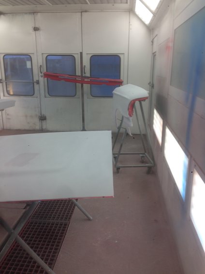 White car fender on a stand inside a paint booth