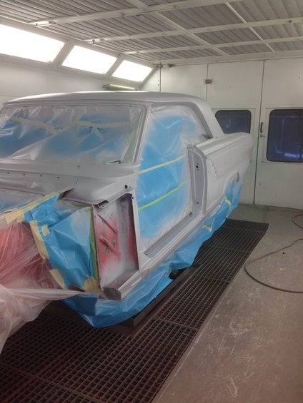 1964 Ford Fairlane body, primed and masked in a paint booth, viewed from the front three-quarter angle