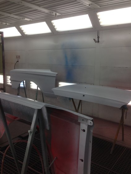 Car fender and hood, primed white, in a paint booth